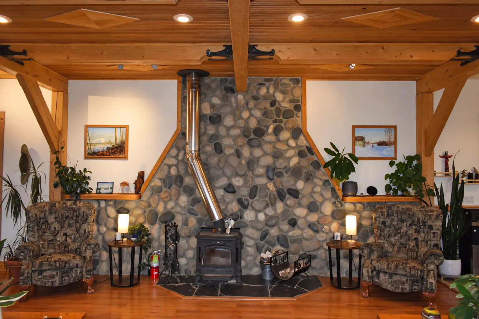 River-stone fireplace wall with a wood stove and armchairs in the shared lounge at Denali Overlook Inn