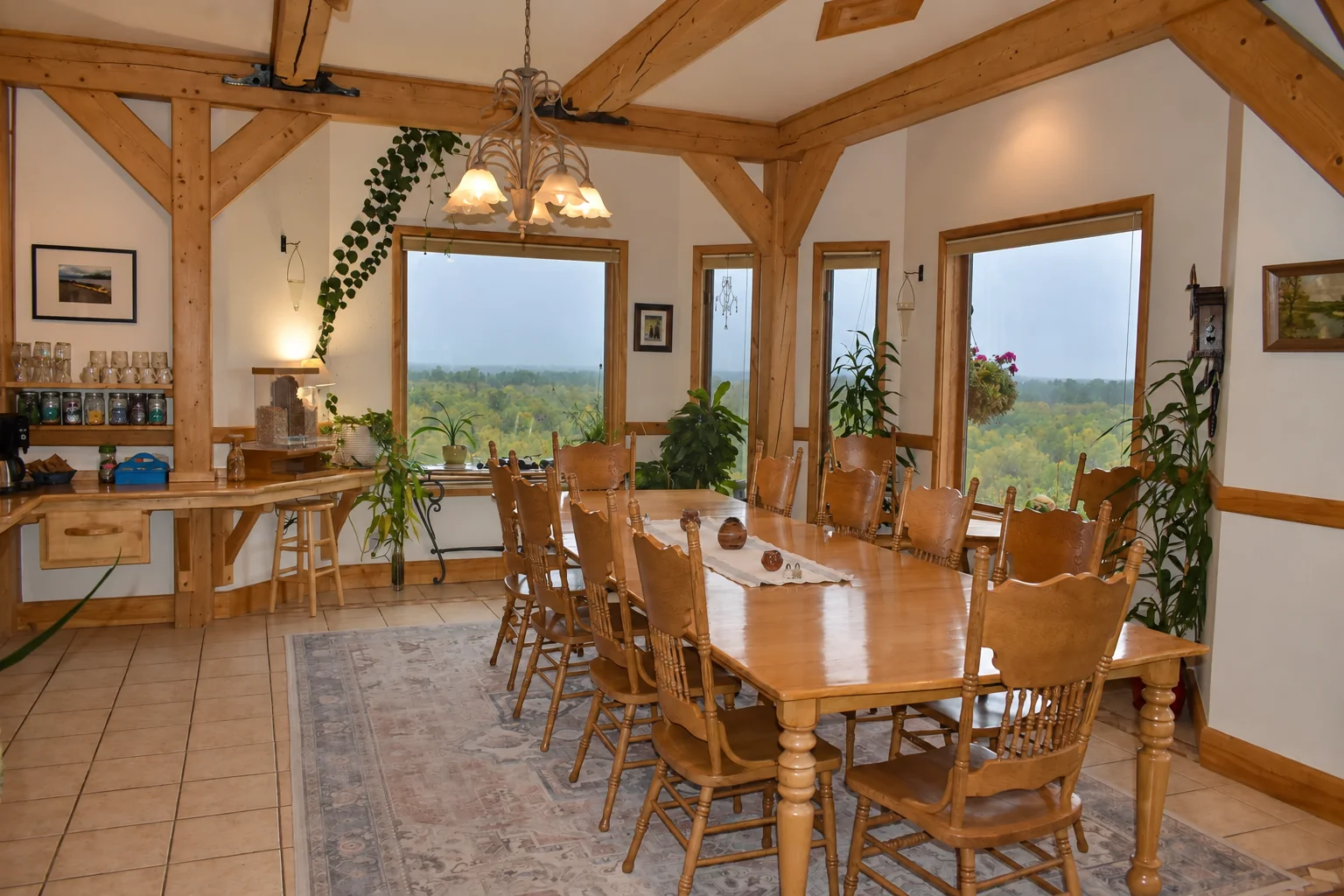 Dining room with a long wooden table, chandelier and windows over the Alaska landscape at Denali Overlook Inn
