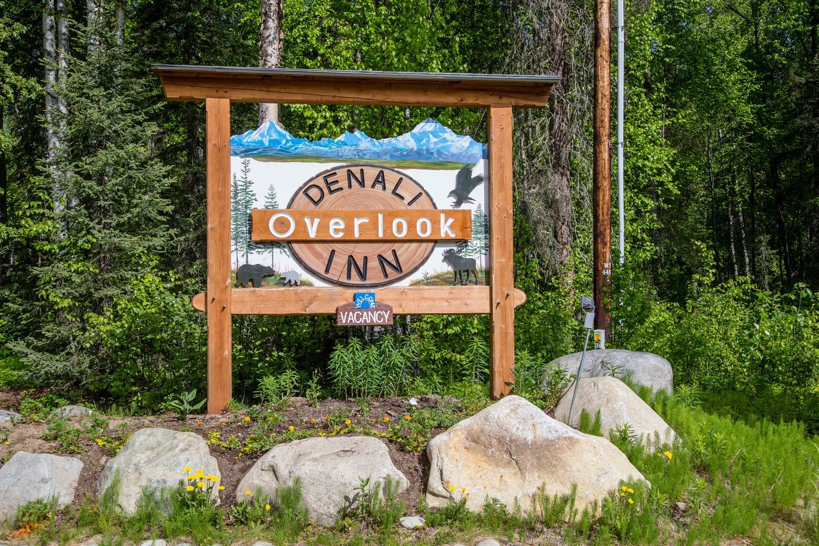 The carved Denali Overlook Inn entrance sign among trees and boulders.